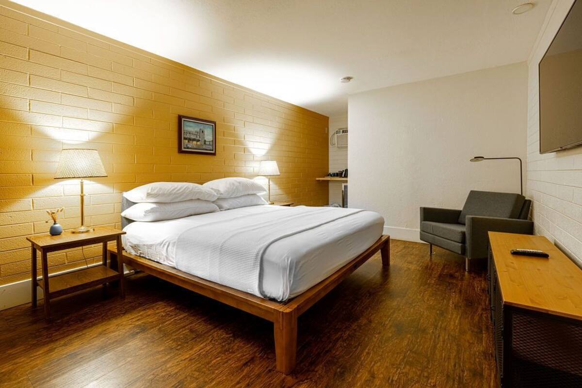 A room with a wooden bed, a small table, a chair, and a TV.