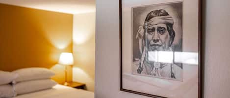 A hotel room with a bed, a nightstand with a lamp, and a framed portrait on the wall.