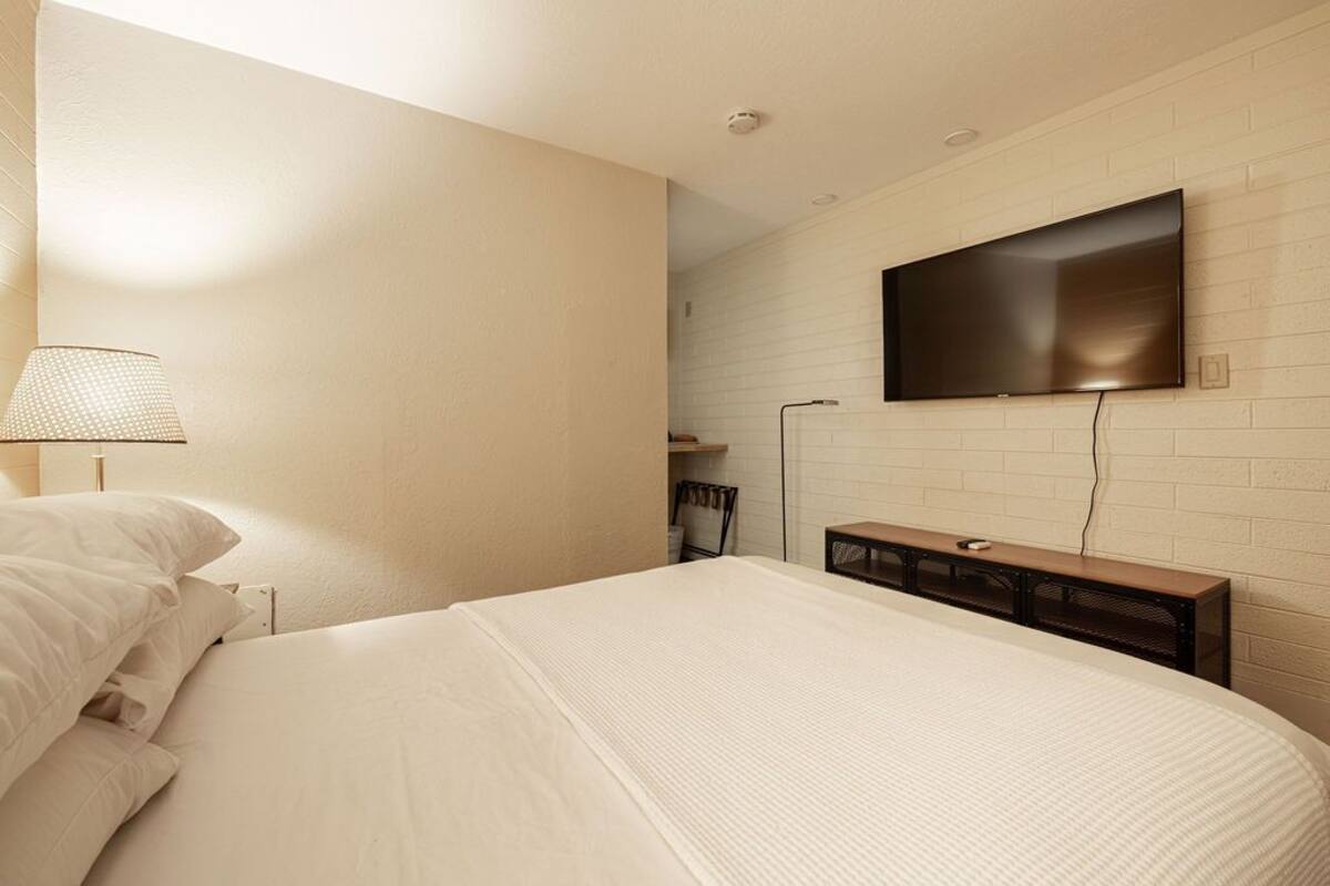A hotel room with a large bed, a flat-screen TV mounted on the wall, a bedside table, and a lamp.