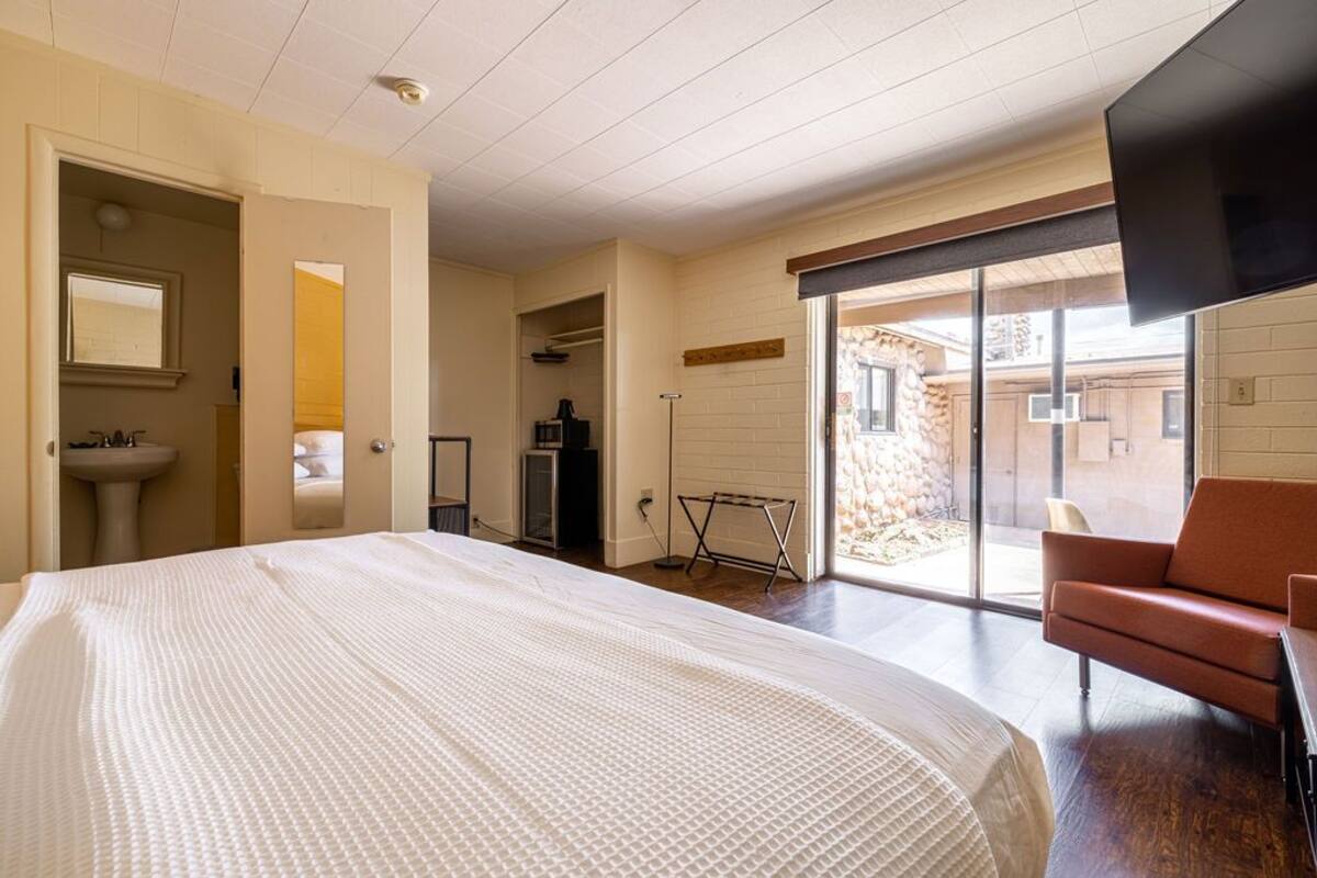 A bedroom with a large bed, a bathroom, a seating area, and a sliding glass door to an outdoor space.