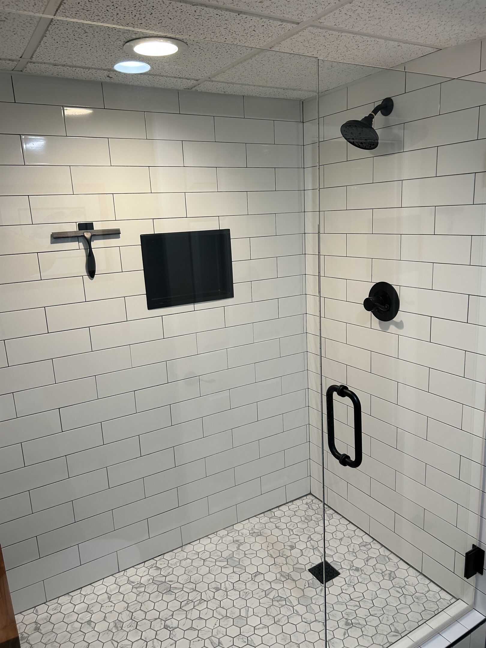 Una ducha moderna con paredes de azulejos blancos y suelo de baldosas hexagonales.