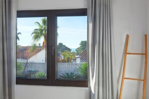 Una habitación con ventana que da a un jardín, una escalera de madera y una pared blanca.