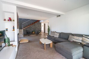 A modern living room with a grey sofa, a coffee table, and a staircase with a stone wall. - Modern Villa close to Costabella beach (Marbella)