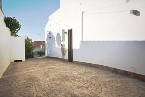 A paved courtyard with a white building, a door, and a small wall-mounted device.
