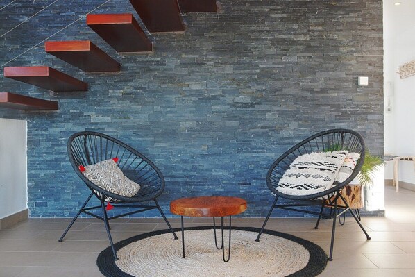 A modern interior with a stone wall, two black wire chairs with patterned cushions, a small wooden table, and a woven rug.