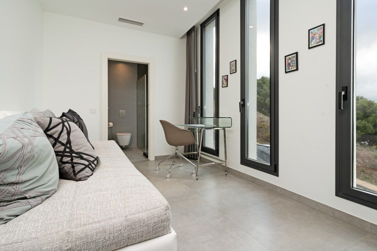 Une chambre moderne avec un canapé, une table en verre et une vue dégagée sur l’extérieur grâce à de grandes fenêtres.
