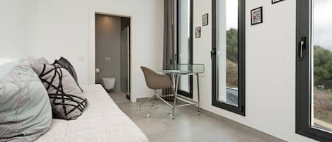 Une chambre moderne avec un canapé, une table en verre et une vue dégagée sur l’extérieur grâce à de grandes fenêtres.