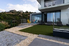 Ein modernes Haus mit Glasfassade, Sitzgelegenheit im Freien und einem angelegten Garten.