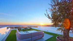Una terraza en la azotea con un sofá, un árbol en maceta y vistas al atardecer sobre el océano.
