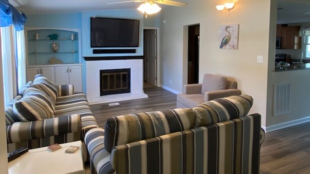 A living room with striped sofas, a flat-screen TV, a fireplace, and a ceiling fan.