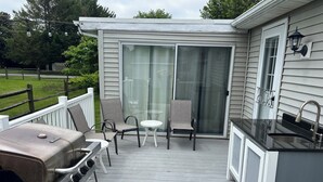 A covered outdoor deck with a barbecue grill, a small table, and chairs.