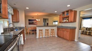 A modern kitchen with wooden cabinets, a central island, bar stools, and a dining area.