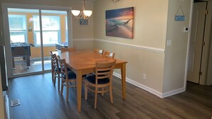 A dining area with a wooden table and chairs, a painting on the wall, and a view through a glass door.