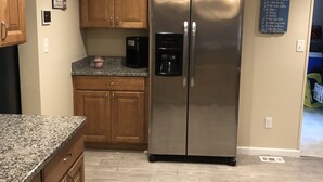 A kitchen with granite countertops, wooden cabinets, a stainless steel refrigerator, and a coffee maker.