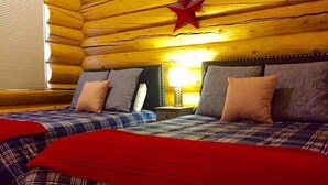Una habitación tipo cabaña de madera con dos camas, ropa de cama escocesa, una decoración con una estrella roja y una mesita de noche con lámpara.