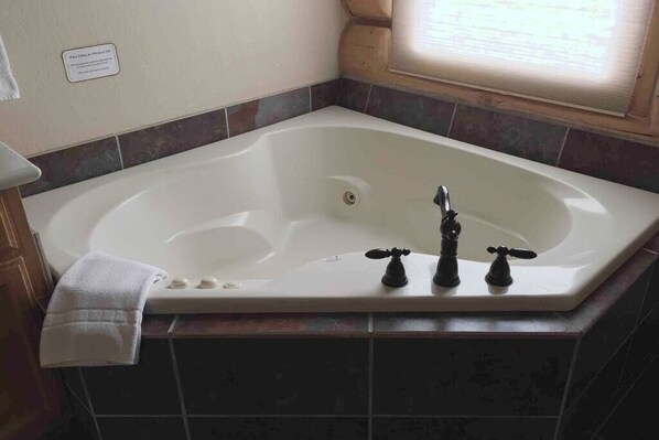 A large bathtub with three faucets, a towel, and a window with blinds. - Greer Riverside Lodge #174-Log Cabin (Greer)