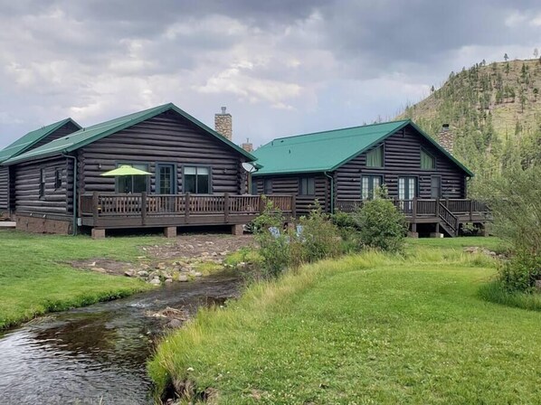 A log cabin with a green roof, a porch, and a stone chimney. - Greer Riverside Lodge #174-Log Cabin (Greer)
