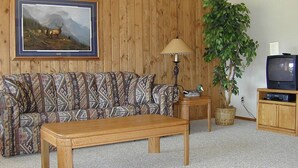 A living room with a patterned sofa, a wooden coffee table, a lamp, a television, and a large plant. - (1)Big Sky 2BR Condo w/outdoor heated pool/hot tub (Big Sky)