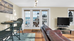 A living room with a chessboard, a leather couch, a TV, and a view of a building through glass doors.