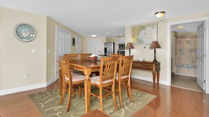 A dining area with a wooden table and chairs, a kitchen in the background, and a map on the wall.