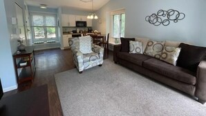 A spacious living area with a sofa and armchair, a kitchen in the background, and a decorative wall piece. - Beach, Boat Rentals, Near Horse Shows! RIverside Shores (Williamsburg)