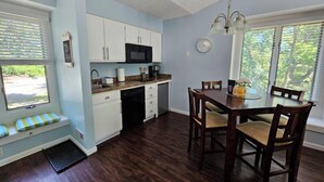 A compact kitchen with white cabinets, a black microwave, and a dining area with wooden chairs and a glass table. - Beach, Boat Rentals, Near Horse Shows! RIverside Shores (Williamsburg)