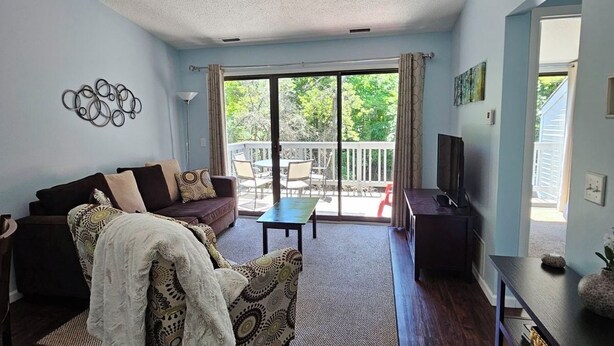 A living room with a sofa, armchair, coffee table, TV, and a balcony with outdoor furniture. - Beach, Boat Rentals, Near Horse Shows! RIverside Shores (Williamsburg)