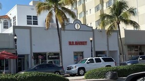 Un immeuble commercial avec une enseigne indiquant « MB MARKET » et des palmiers devant.