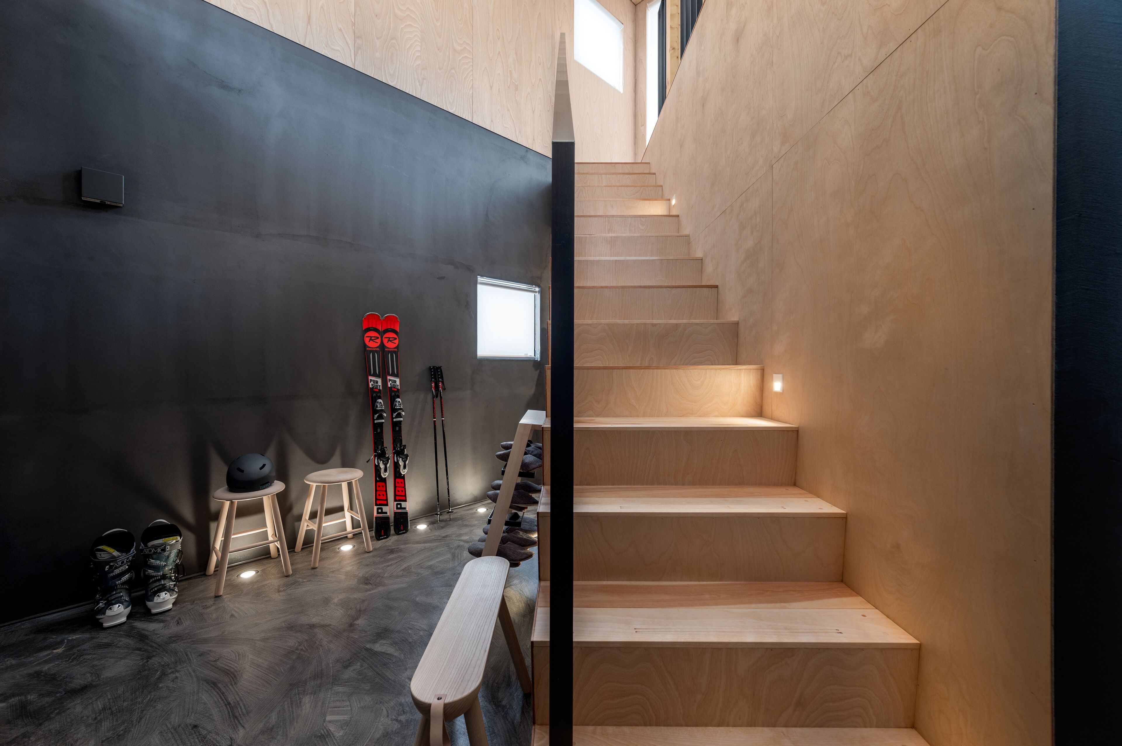 A modern interior with a staircase, wooden flooring, and ski equipment.