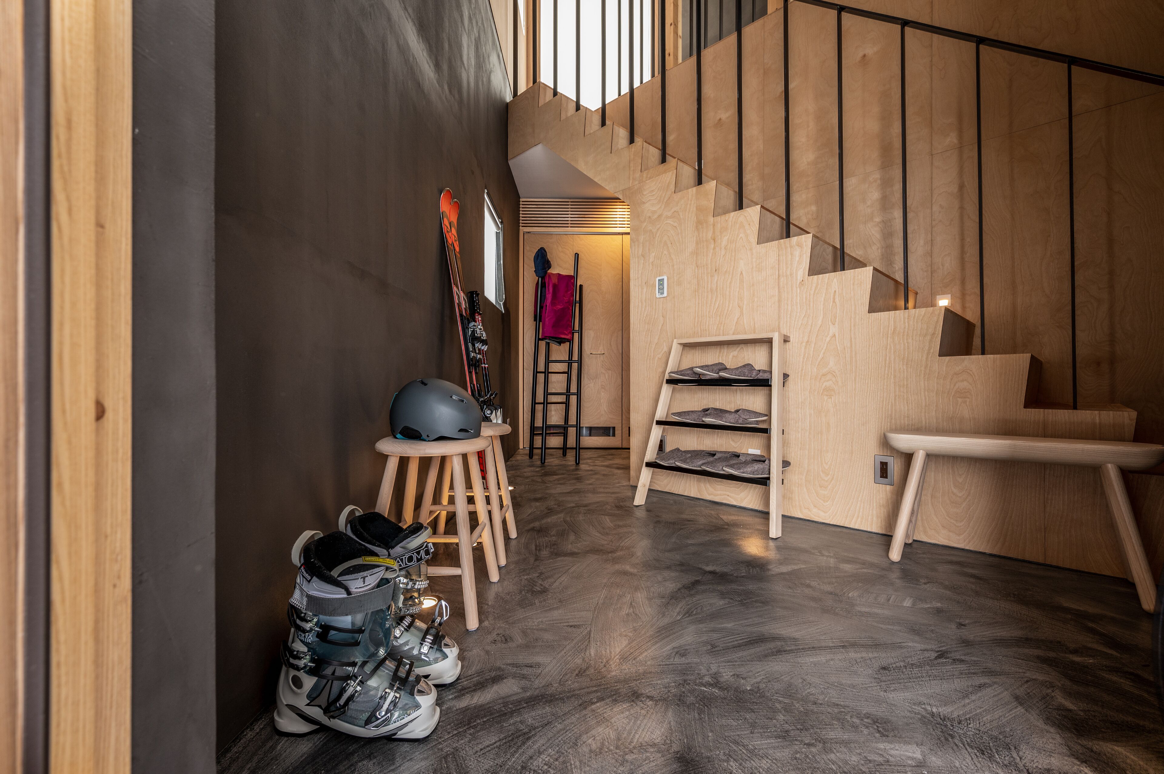 Una escalera de madera que lleva al segundo piso, un zapatero y un par de esquíes apoyados en la pared.