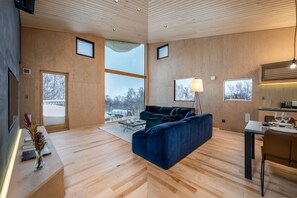 A modern living room with a blue sofa, wooden flooring, and large windows offering a view of a snowy landscape.
