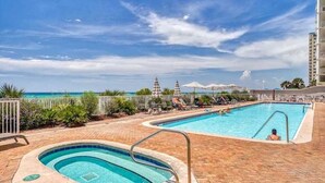 Zona de piscina con hidromasaje, sillas de descanso y sombrillas, con vista a la playa.