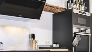 A modern kitchen with a black range hood, stainless steel appliances, and a wooden cutting board. - Duplex Standing de 77m2 Avec Rooftop de vue mer Situé Plein Centre de Bandol (Bandol)