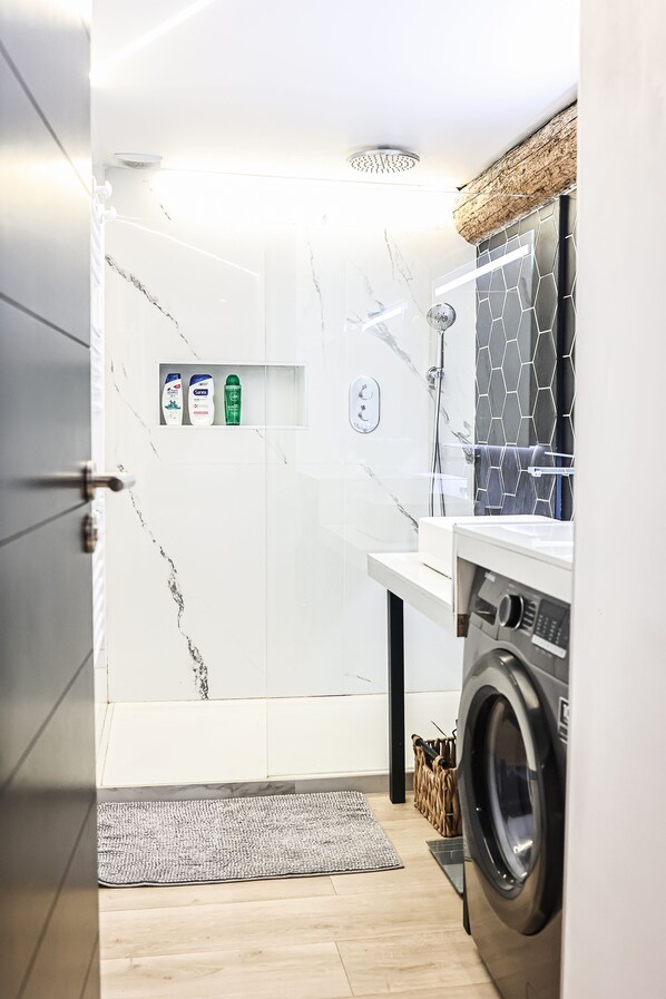 A modern bathroom with a shower, a built-in washing machine, and a shelf with toiletries. - Duplex Standing de 77m2 Avec Rooftop de vue mer Situé Plein Centre de Bandol (Bandol)