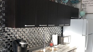 A modern kitchen with dark cabinets, a marble backsplash, a Keurig coffee maker, a sink, and a white refrigerator. - Hollywood Art Studio Apartment (Los Angeles)