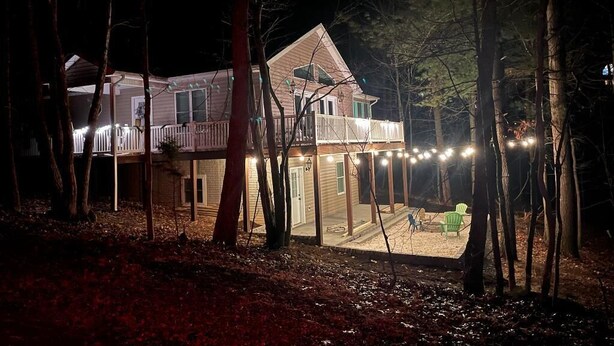 Una casa de dos pisos con un balcón, rodeada de árboles e iluminada con luces colgantes.