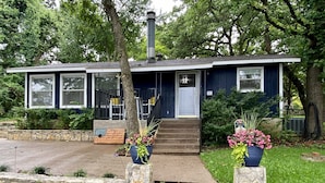 A single-story house with a front porch, a chimney, and a small garden area with potted plants. - Cozy Lakefront Cottage on Eagle Mountain Lake (Azle)