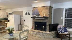 A living room with a stone fireplace, a dining table with chairs, a TV, and a patterned rug. - Cozy Lakefront Cottage on Eagle Mountain Lake (Azle)