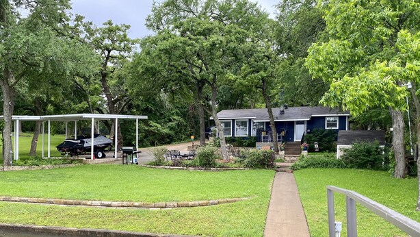 A house with a covered patio, a wooden dock extending over a body of water, and a grassy yard with trees. - Cozy Lakefront Cottage on Eagle Mountain Lake (Azle)