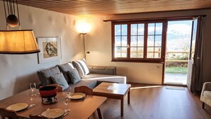 A dining area with a wooden table set for four, a sofa with cushions, and a large window with a view of the outdoors. - Wohnung Nr.2 by Interhome (Schluein)