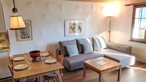 A modern living room with a wooden dining table, a sofa, and a coffee table. There are two wall-mounted lamps and a framed picture on the wall. - Wohnung Nr.2 by Interhome (Schluein)