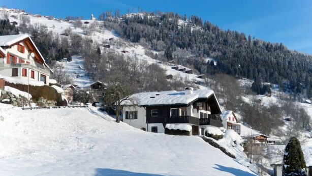 A snow-covered mountain village with traditional wooden houses, a clear blue sky, and a forested hillside. - Wohnung Nr.2 by Interhome (Schluein)