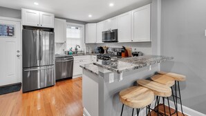 A modern kitchen with white cabinetry, stainless steel appliances, a granite countertop, and wooden bar stools. - ★ Stunning 3BR Modern Charm in South Philly ★ (Philadelphia)