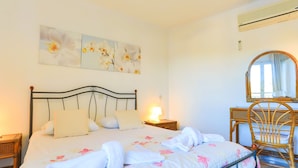 Een net opgemaakt bed met bloemenbedrukking, een bedlampje, een houten stoel en een spiegel aan de muur.