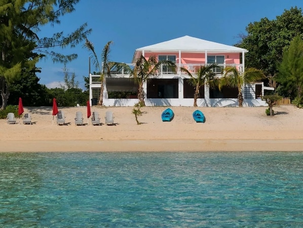 A beachfront property with a white building, beach chairs, and two boats. - Trela Sands is a 3 Bedroom Unit with generator, right on a sandy beach (South Palmetto Point)