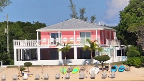 Una propiedad frente al mar con una casa de dos pisos, un balcón y una fila de sillas de playa y kayaks.