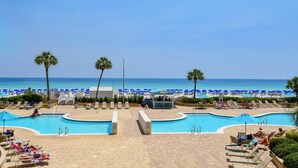 A pool area with lounge chairs and a beach in the background.