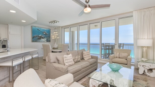 A spacious living room with a large sofa, a glass coffee table, and a view of the ocean through large windows.