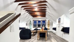 Un espacio tipo loft con vigas de madera a la vista, piso de madera, una mesita y un sillón de peluche.