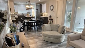 Un soggiorno moderno con un divano beige rotondo, un'area pranzo con tavolo e sedie in legno, e una cucina sullo sfondo.